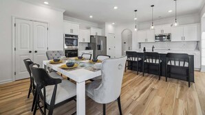 A modern kitchen with white cabinetry, a dining table with chairs, and a bar area. - Fort Haven Near Fort Campbell, Spacious 4BR Retreat (Clarksville)