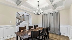 A dining room with a wooden table, chairs, a chandelier, and a staircase in the background.