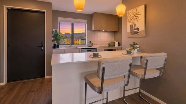 A modern kitchen with a central island, bar stools, pendant lighting, and a view of a sunset.