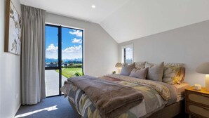 A bedroom with a large bed, a nightstand, a window with a view of mountains, and a door leading to a balcony.
