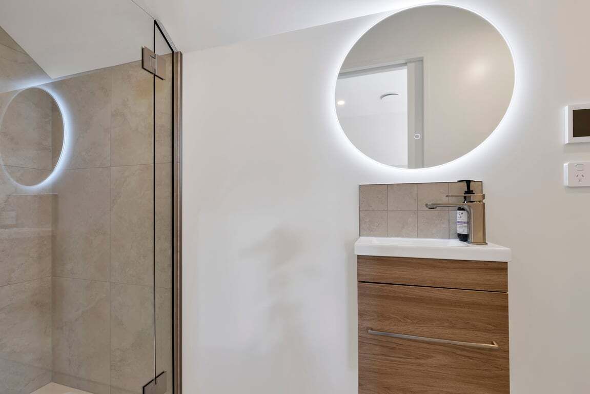 Une salle de bain moderne avec une douche à parois de verre, un miroir rond et un meuble-lavabo en bois.