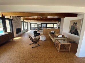 Ein geräumiger Wohnbereich mit Holzbalkendecke, Kamin, einer Couch, einem Esstisch und einer Küchenzeile.