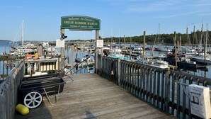 A wooden dock with a sign welcoming to Dysart's Great Harbor Marina, a marina with boats, and a wooden cart.