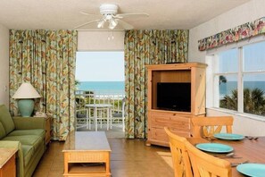 Ein Zimmer mit Fernseher, Esstisch mit Stühlen, einer Couch und Vorhängen.