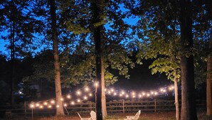 Un espace extérieur aménagé avec des guirlandes lumineuses, un foyer et une terrasse en pierre.
