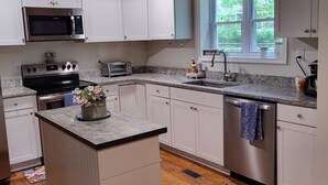 Une cuisine avec des meubles blancs, un four à micro-ondes, un grille-pain, un évier et une fenêtre.