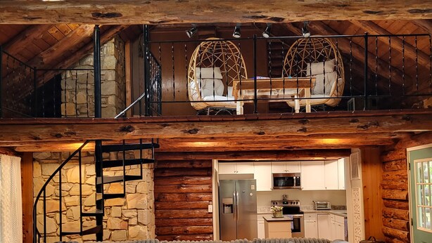 L’intérieur chaleureux d’un chalet avec un plafond en bois, un mur en pierre, un coin repas et un canapé agrémenté de coussins à motifs floraux.