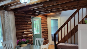L’intérieur d’une cabane en rondins, avec un coin repas, un escalier en bois et une vue à travers une porte.