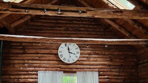 L’intérieur d’une cabane en rondins, avec un plafond en bois, une horloge, un téléviseur et une fenêtre avec des rideaux.