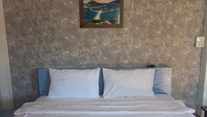A hotel room with a bed, pillows, a painting of a coastal scene, and towels on the bed. - Phum Riang House (Chaiya)