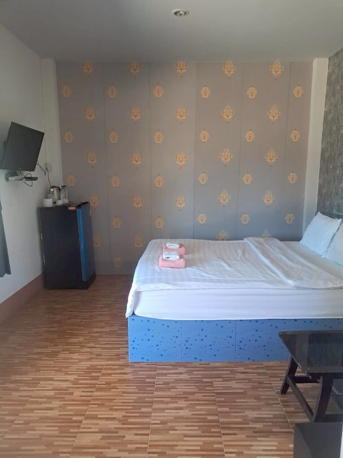 Une chambre d’hôtel avec un lit, un bureau, un téléviseur fixé au mur et un papier peint à motifs.