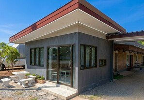 A modern building with large windows, a covered patio area, and outdoor seating. - Phum Riang House (Chaiya)