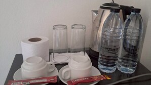 A table with a coffee maker, two water bottles, a cup, a saucer, a roll of paper towels, and two packets of Nescafe coffee. - Phum Riang House (Chaiya)