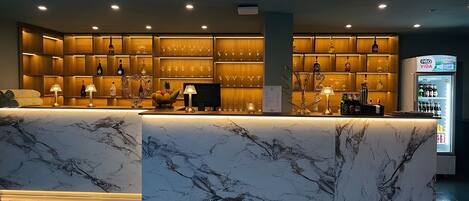 Zona de bar con mostradores de mármol, estanterías con botellas y vasos, y un refrigerador con el rótulo 'DRO VIDA'.