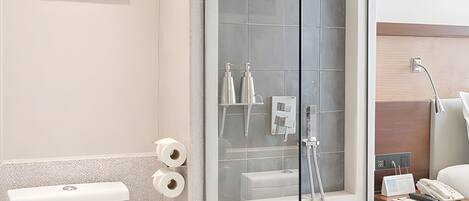 A modern bathroom with a glass-enclosed shower, a toilet, a trash bin, and a framed artwork on the wall.