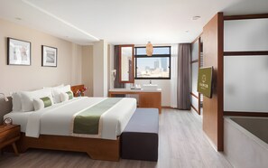 Habitación de hotel con cama, mesita de noche, escritorio y vista a la ciudad a través de una ventana.