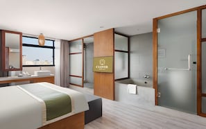 Habitación de hotel con cama, baño con bañera, espejo grande y vista a la ciudad.