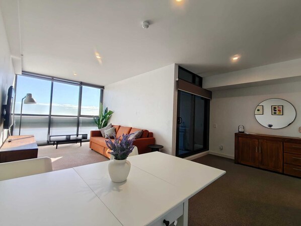 A modern living room with a white table, a sofa, a large window, and a view of the ocean. - Apartment in Adelaide CBD with parking (Adelaide)