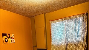 Quarto de hotel com uma cama, uma obra de arte na parede, uma janela com cortina estampada e uma cabeceira.