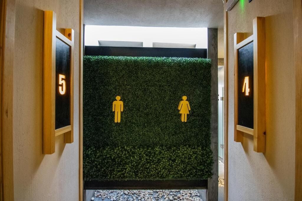 Un pasillo con pared verde, puertas numeradas y una pequeña zona de piedrecitas al final.