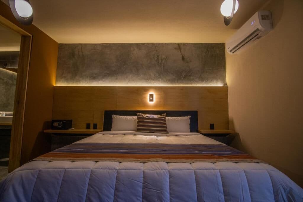A hotel room with a large bed, bedside tables, a wall-mounted light, and an air conditioning unit.