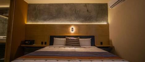 A hotel room with a large bed, bedside tables, a wall-mounted light, and an air conditioning unit.