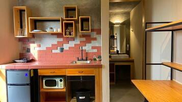 Una cocina compacta con microondas, un refrigerador pequeño y estantes de madera.
