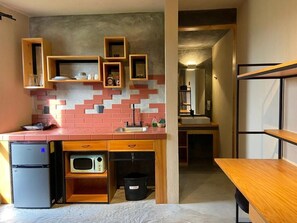 Una cocina compacta con microondas, un refrigerador pequeño y estantes de madera.
