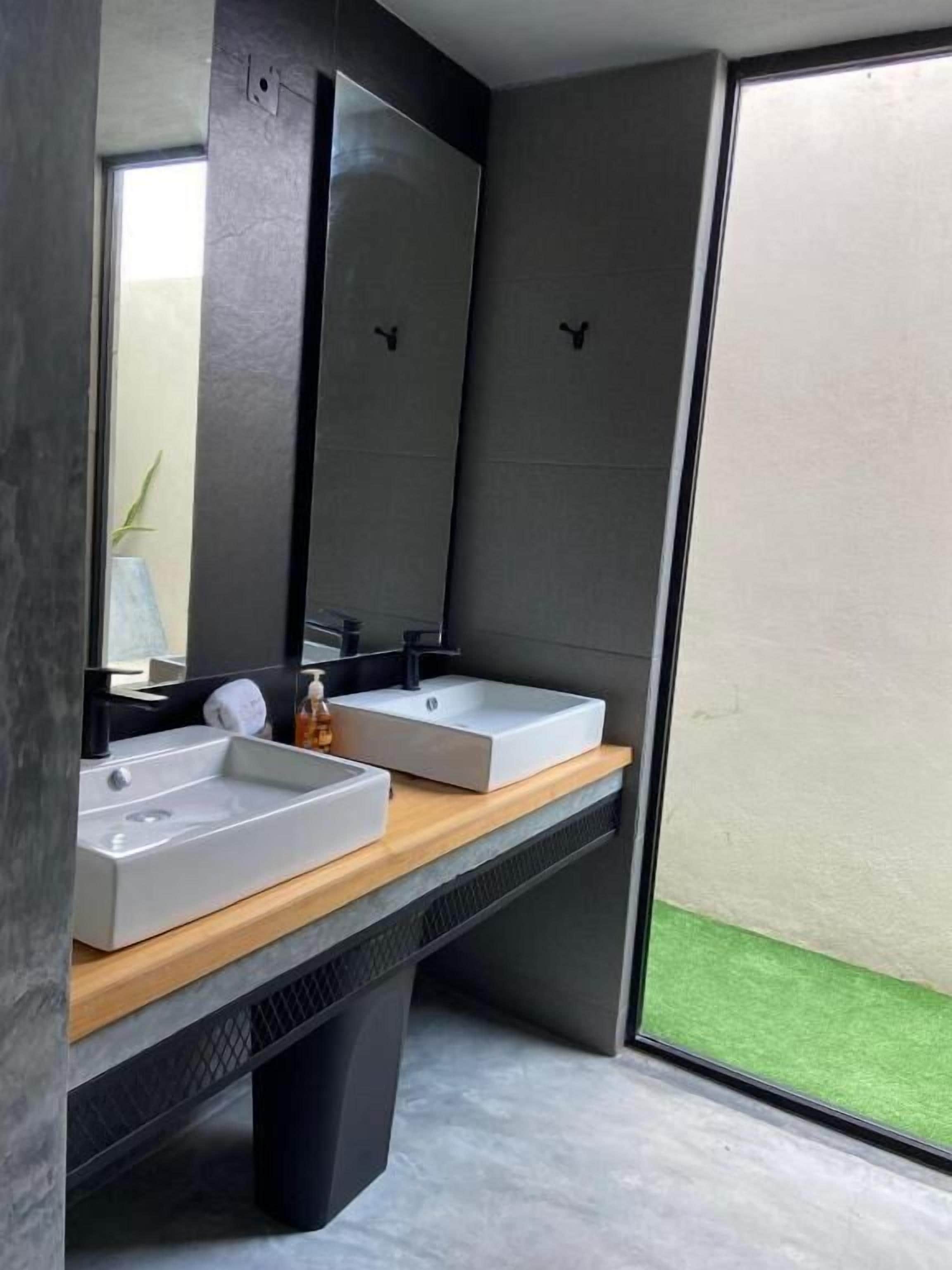 A modern bathroom with two sinks, a large mirror, and a view of a green outdoor area.