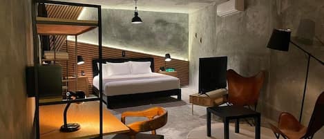 A modern hotel room with a bed, desk, chair, TV, and a unique ceiling design.