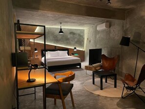 A modern hotel room with a bed, desk, chair, TV, and a unique ceiling design.