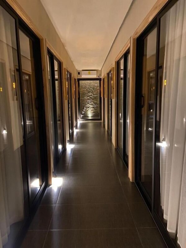 A corridor with doors leading to rooms, a tiled floor, and a view of a body of water through the doors.