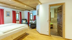 Quarto com uma cama, duas poltronas, uma televisão e uma porta de madeira que dá para um banheiro.