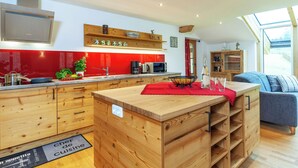 Uma cozinha moderna com armários de madeira, painel de fundo vermelho e uma área de jantar com sofá azul.