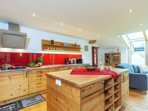 Eine moderne Küche mit Holzausstattung, einer roten Spritzschutzwand und einem Essbereich mit einem blauen Sofa.