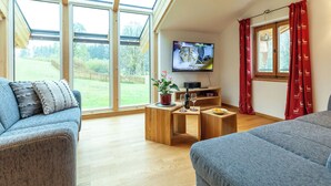 Uma sala de estar moderna com uma televisão grande, móveis de madeira e vista para um jardim.