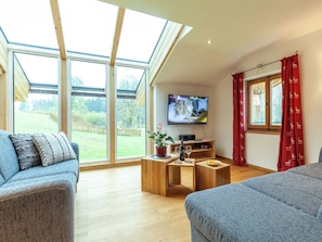 Ein modernes Wohnzimmer mit großem Fernseher, Holzmöbeln und Blick auf einen Garten.