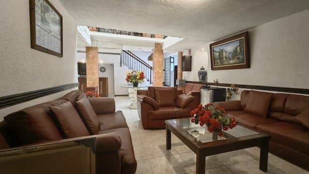 A spacious living room with leather sofas, a coffee table with flowers, and a staircase leading to an upper floor. - hotel avenida  (Zacatlán)