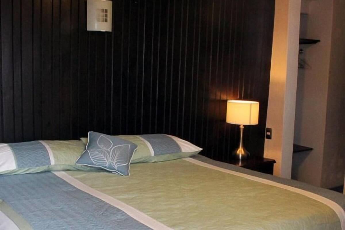 Habitación de hotel con cama, mesita de noche, lámpara y lámpara de pared.