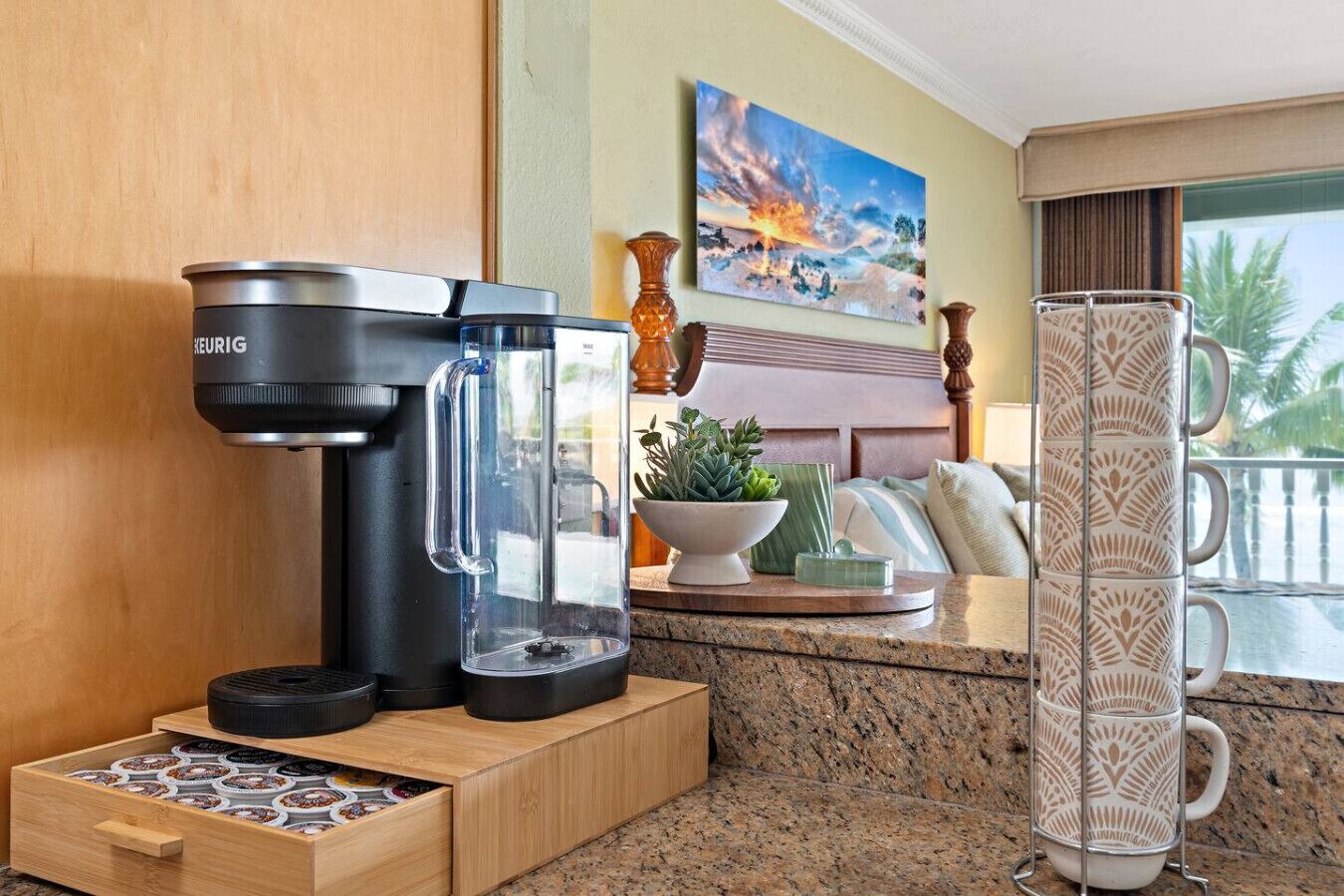 Une cuisine moderne équipée d’une machine à café Keurig, d’une verseuse en verre, d’une cafetière, d’une pile de tasses et d’un tiroir contenant des dosettes de café.