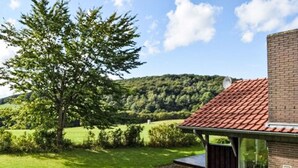 Een modern huis met een rode dakbedekking, omringd door een verzorgd gazon en een grote boom.