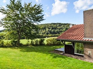 Ein modernes Haus mit rotem Ziegeldach, umgeben von einer gepflegten Rasenfläche und einem großen Baum.