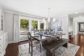 Ein modernes Esszimmer mit einem großen Tisch, gedeckt für sechs Personen, einem Kronleuchter und Blick ins Freie.