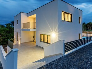 A modern two-story building with a balcony, large windows, and a well-lit entrance. - Vacation home Antica by Interhome (Rab/Lopar)