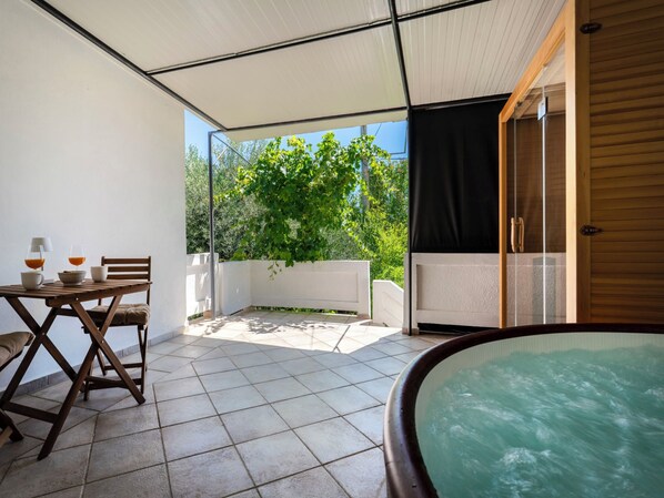 A covered outdoor area with a table, chairs, and a hot tub.