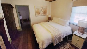 Un dormitorio con cama, mesita de noche, lámpara y un cuadro en la pared.
