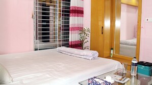 Habitación de hotel con cama, una mesita de vidrio con artículos de aseo, un espejo y una ventana con persianas.