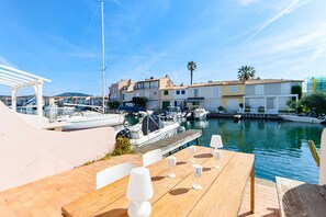 Ein Yachthafen mit Booten, ein Holzdeck mit Tischen und Stühlen sowie Gebäude im Hintergrund.