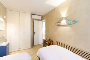 Une chambre avec deux lits, une armoire, une commode, un luminaire fixé au mur et un panneau décoratif sur le thème de la plage.