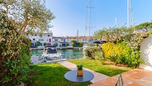 A patio with a table and chairs, a small garden, and a view of a canal with boats and buildings in the background. - PORT GRIMAUD: Superb 3-room apartment - A/C, terrace and garden (PORT GRIMAUD)